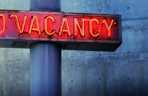 Glowing retro neon 'no vacancy' sign against cool blue wall background